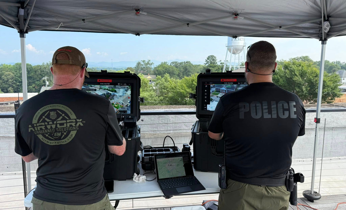 Two police officers operating surveillance equipment under a tent with a scenic background.